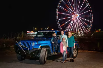 family posing with blue jeep in front of the island wheel