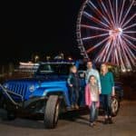 family posing with blue jeep in front of the island wheel