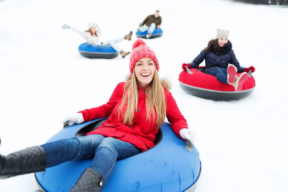 4 smiling people tubing down snowy hill
