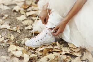 bride tying white sneakers on leaf-covered ground